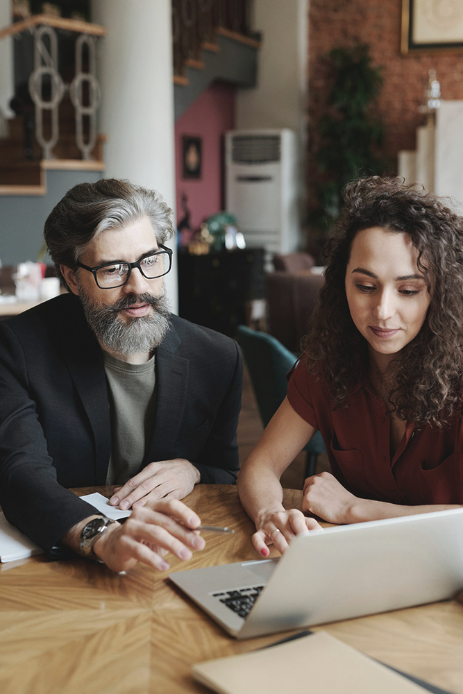 Two professionals using the Xink platform on a laptop, collaborating at a wooden table in a modern office setting.